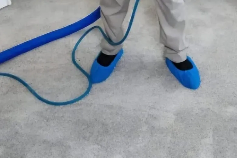 A technician's blue disposable shoe covers and a coiled blue hose resting on pale carpet